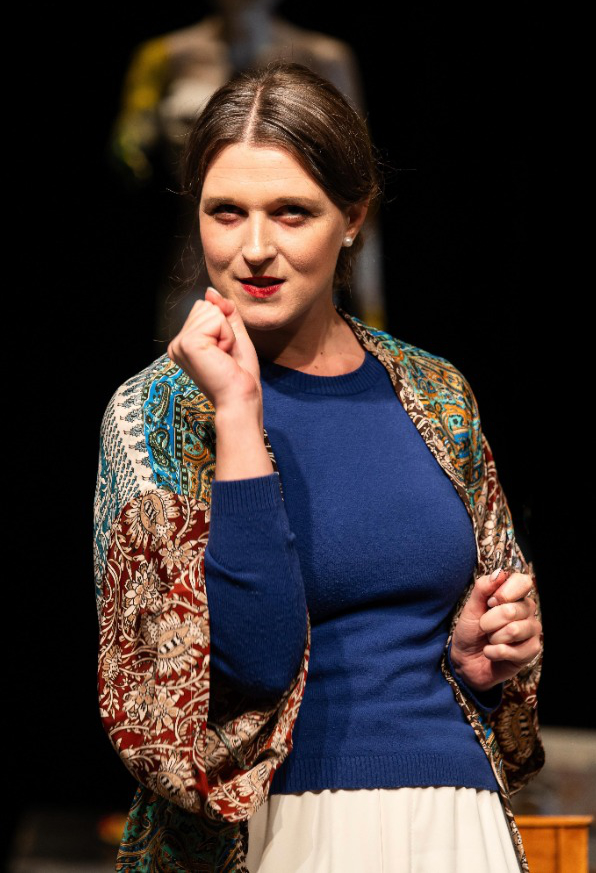 Das Profil einer Theaterdarstellerin mit langem Haar vor schwarzem Hintergrund.